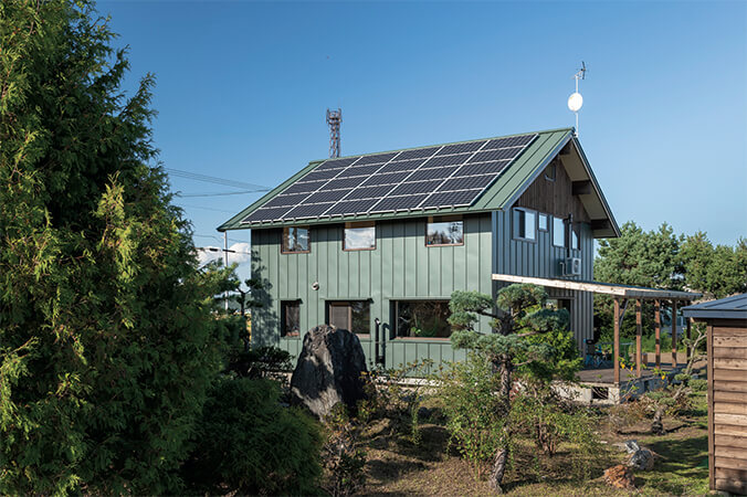 「風景に溶け込むようなみどりの家にしたい」と手描きのスケッチを持参したKさんの希望を叶えた、深い緑色のガルバリウム鋼板とカラマツを組み合わせた外観。屋根一面の太陽光発電パネルがつくり出すエネルギーで、暮らしで消費するエネルギーのほとんどをまかなっている